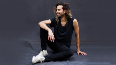 Man wearing all black and white converse sneakers sitting on black drape